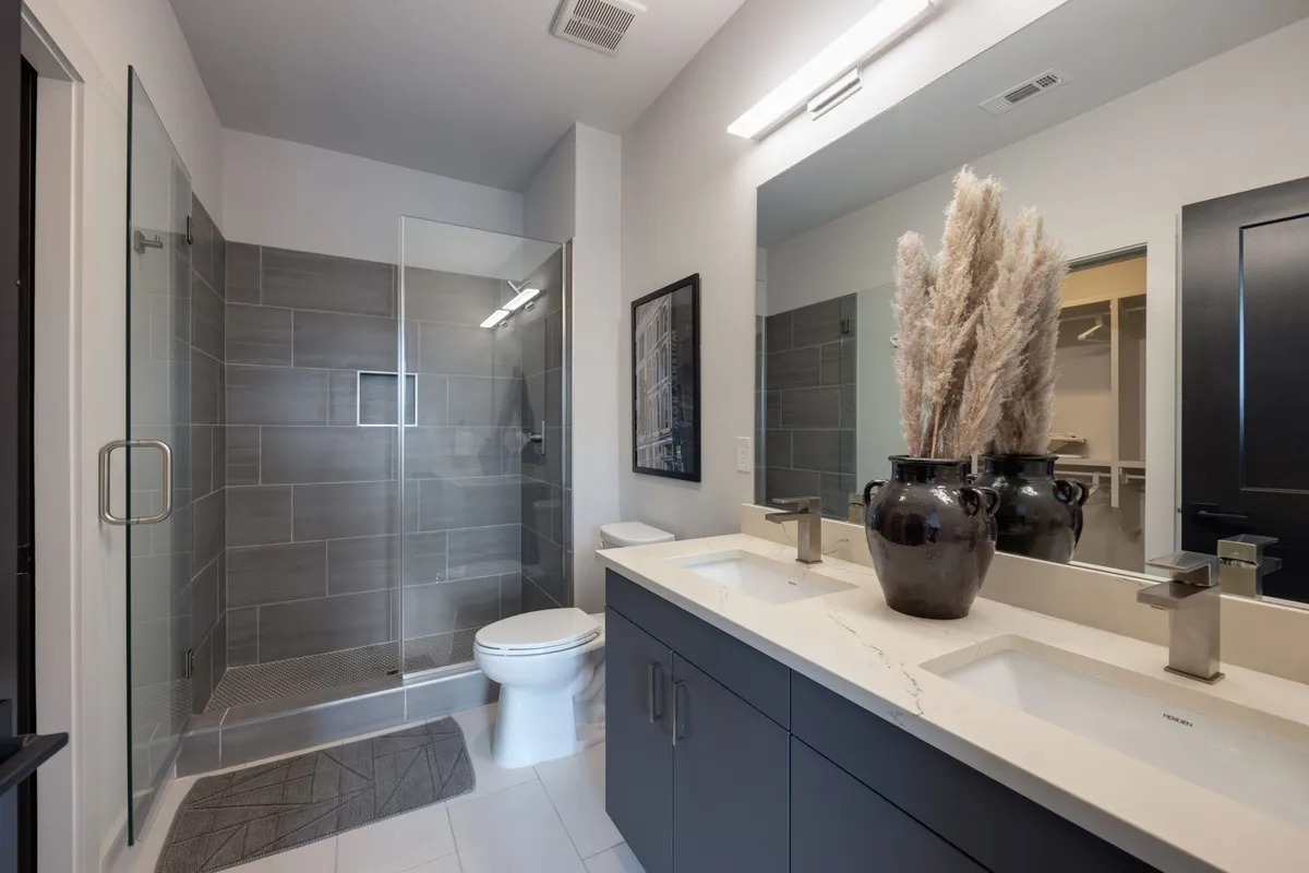A contemporary bathroom with a double sink, large glass shower, stylish decor, and a decorative vase with pampas grass. The space exudes tranquility, ideal for refreshing routines and self-care.