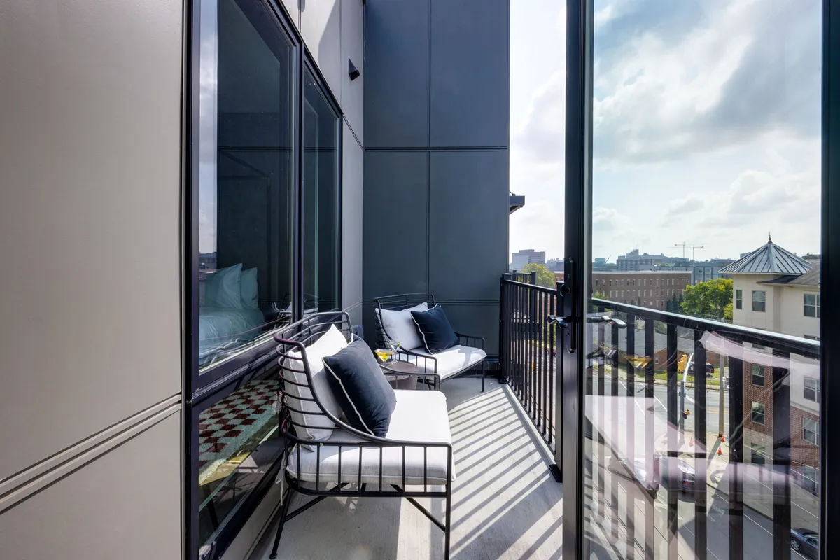 A stylish balcony with comfortable seating and a glass railing, offering a panoramic view of the Nashville city skyline. The scene suggests relaxation after a day out, with the city’s buzz visible from the private vantage point.