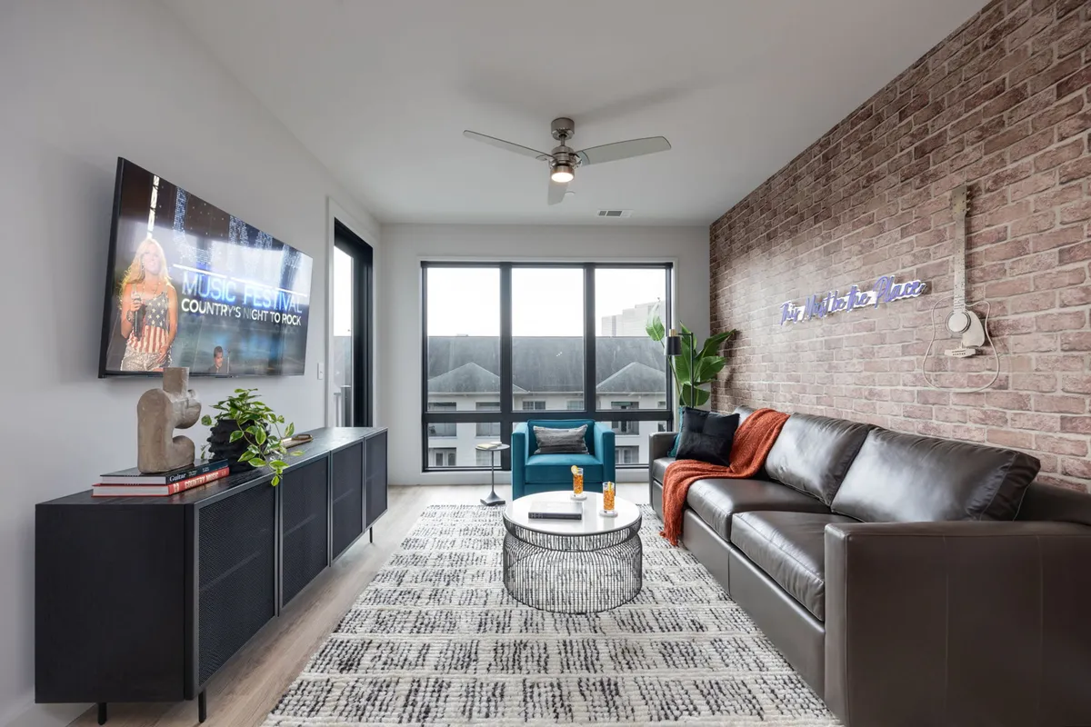 A modern, casual living space with a brown leather sofa, blue accent chair, round coffee table, and a television displaying a music festival. The decorative wall adds interest and urban flair, while the layout supports both relaxation and social events.