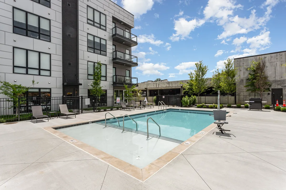 A resort-style pool framed by lush greenery and modern balconies, offering spaces for sunbathing, swimming, or relaxing with friends. The setting is vibrant, social, and perfect for recharging after a night out.