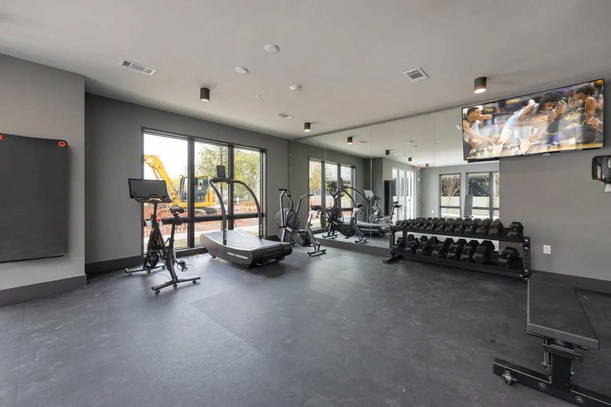 A bright, modern on-site fitness center with state-of-the-art equipment, large windows letting in natural light, and a motivating atmosphere ideal for morning workouts.