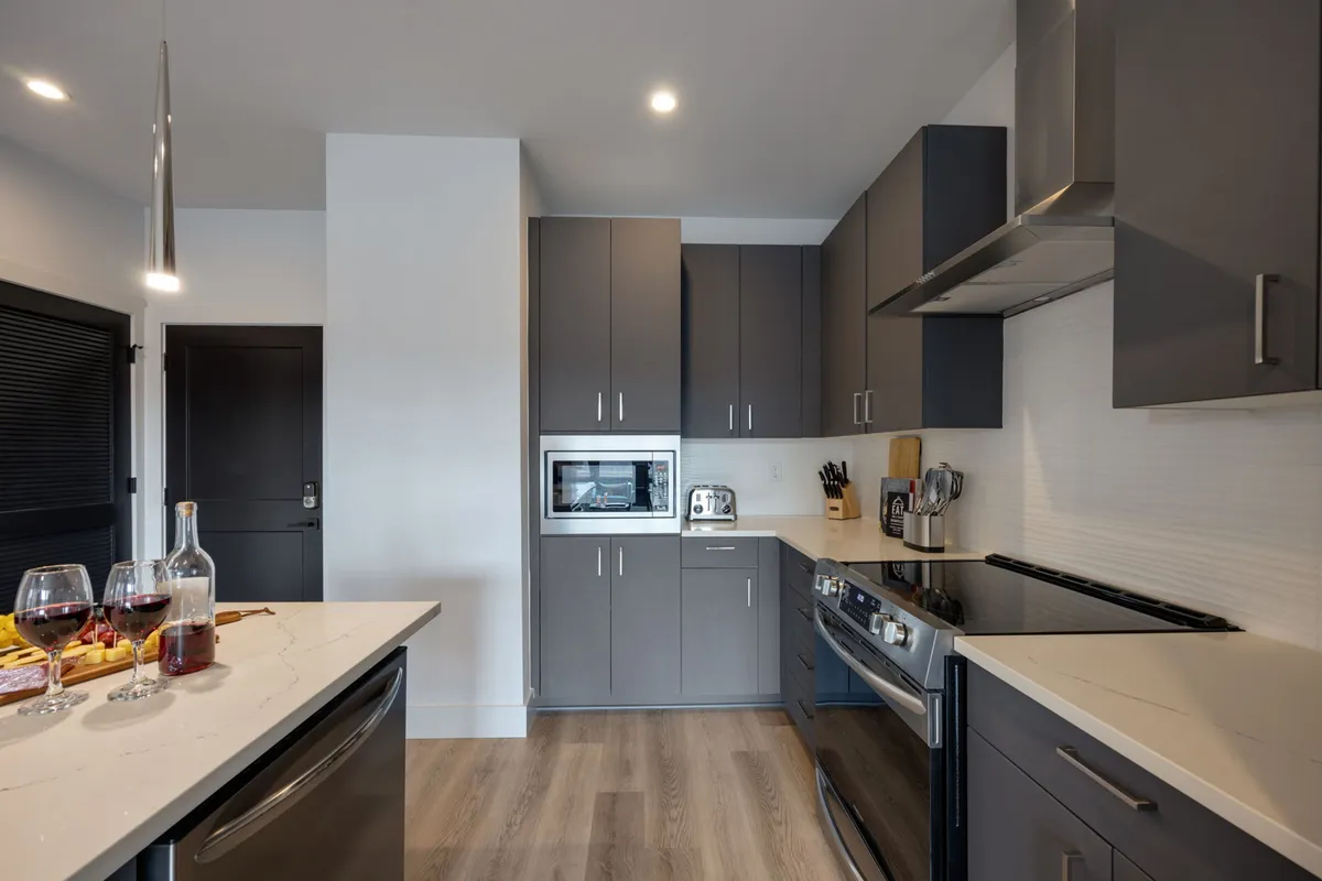 A close-up view of a kitchen island with a sleek countertop, modern stainless steel appliances visible in the background, and wine glasses placed on the surface. The scene evokes warmth and a sense of culinary adventure, highlighting the kitchen's role in entertaining and social gatherings.
