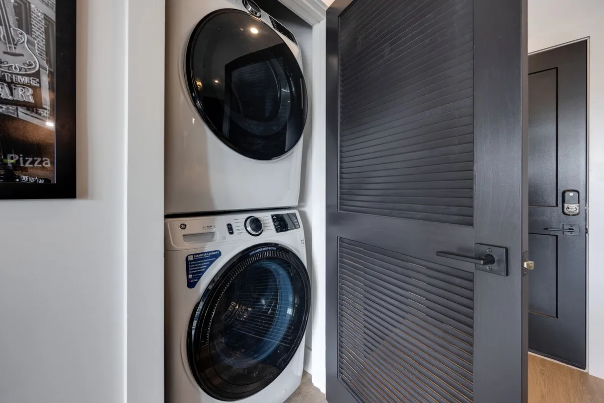 A practical and stylish in-unit laundry area with a washer and dryer unit, framed artwork, and a dark door, conveying efficiency and comfort for daily living.